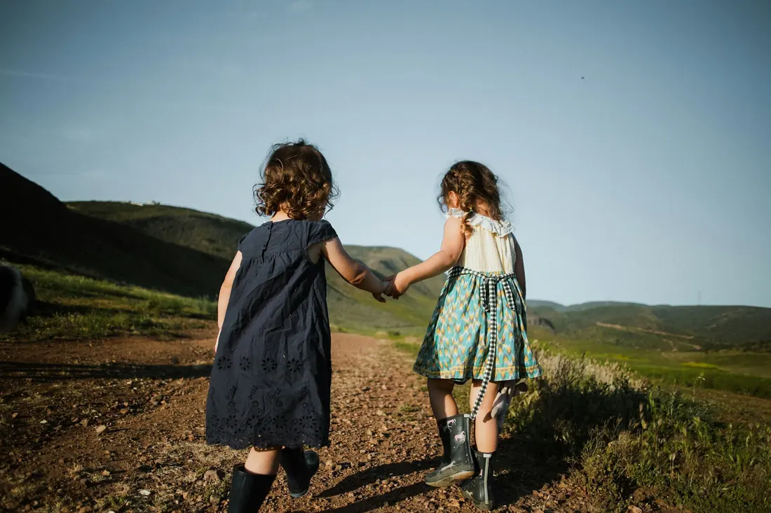 Deux petites filles de dos se tiennent la main sur un chemin de colline.